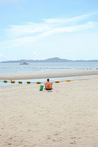 Man sitting on beach against sky