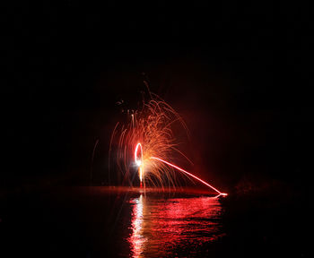 Illuminated firework display over river against sky at night