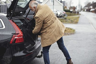 Senior man keeping golf bag in car trunk during winter