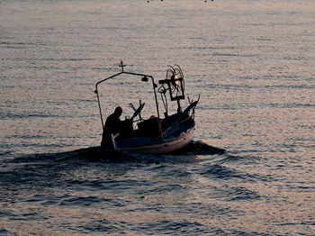 Silhouette people in boat sailing on sea against sky