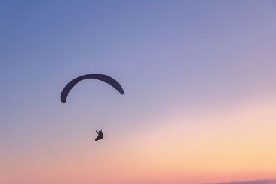 Silhouette person paragliding against sky during sunset