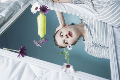 Young woman reflecting in mirror lying on bed