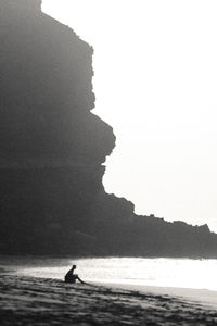 Scenic view of silhouette of a person sitting on the beach by the ocean watching the waves