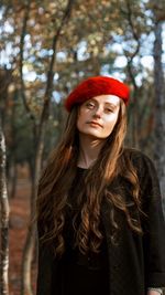 Portrait of young woman wearing red flat cap while standing against trees