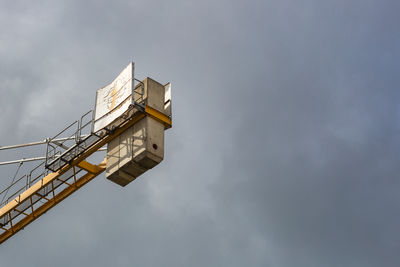 Low angle view of cherry picker against cloudy sky