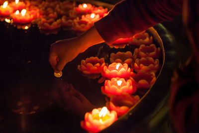 Cropped hand with coin above lit candles in water filled container at temple