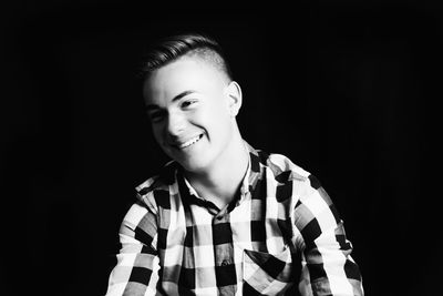 Smiling young man standing against black background