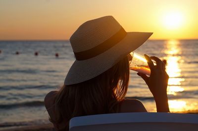 Young woman having drink at beach during sunset