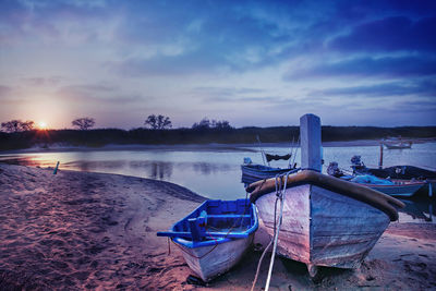 Boat moored at beach against sky during sunset