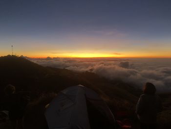 Rear view of man looking at mountains against sky during sunset