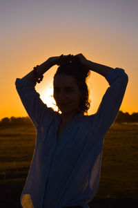 Portrait of woman with arms raised standing against sky during sunset