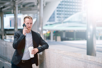 Businessman answering smart phone while standing in city