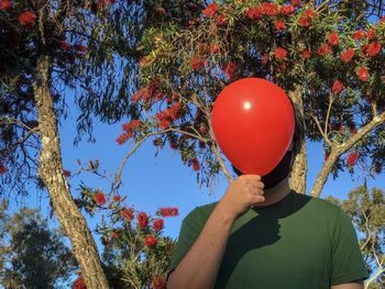 Low angle view of man holding red balloon against flowering tree.