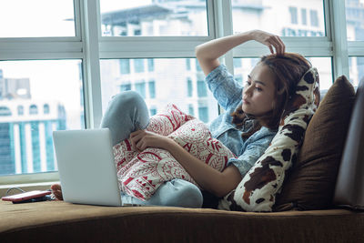 Young woman using phone while sitting on window