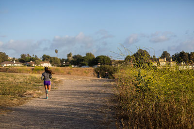 Rear view of boy running on field against sky