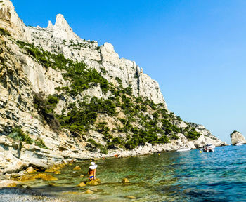People on rock by sea against clear sky