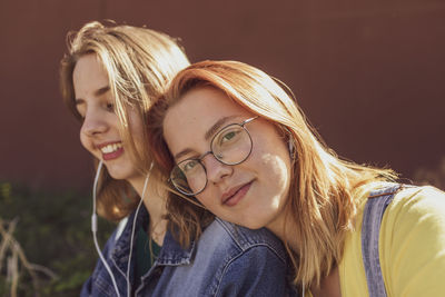 Young woman by friend listening music through in-ear headphones