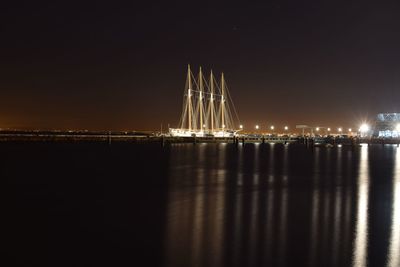 Illuminated city by sea against sky at night