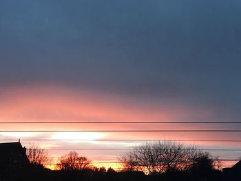 Silhouette trees against dramatic sky during sunset