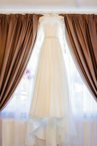 Low angle view of wedding dress hanging on window