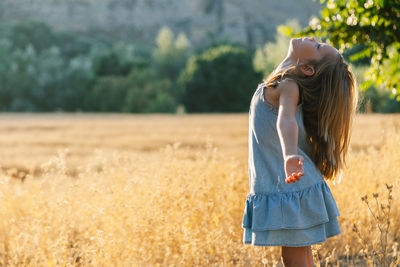 Side view of girl with arms outstretched standing on grassy field