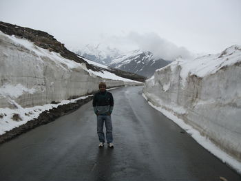 Full length of man standing on road amidst snowcapped mountains