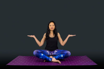 Portrait of young woman sitting against black background