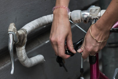 Cropped hands of woman locking bicycle by wall