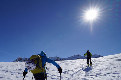 People skiing on snowcapped mountain against blue sky