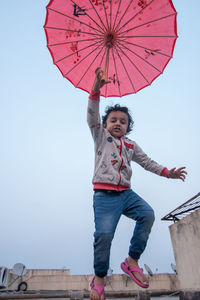 Full length of happy boy standing on umbrella against sky