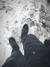 High angle view of a mans black jeans legs and hiking boots in the snow