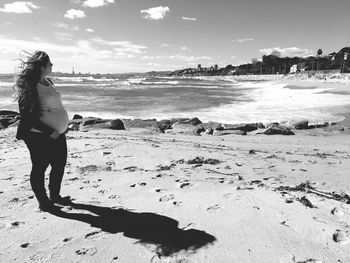 Pregnant woman standing at beach against sky