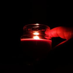 Close-up of hand holding illuminated candle against black background