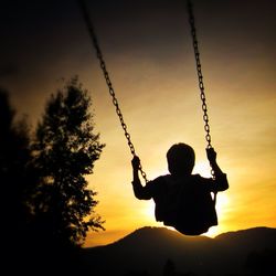 Silhouette of man sitting on swing at playground