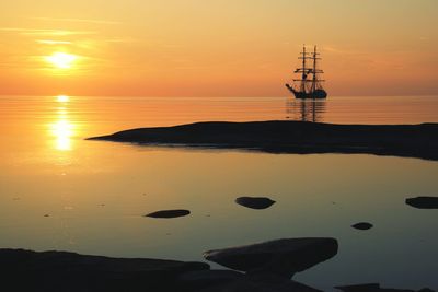 Silhouette sailing ship in sea against orange sky during sunset