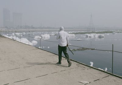 Rear view of woman standing on riverbank during winter