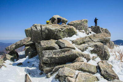 Low angle view of people standing on rock against clear blue sky