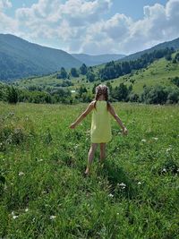 The view of the girl from behind, standing in a green clearing, looking at the mountains.