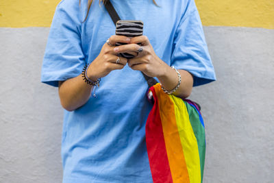 Unrecognizable person using mobile phone while wearing a belt bag with the lgbt rainbow flag.