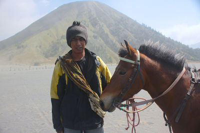 Portrait of young man by horse on field with mt bromo in background