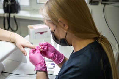 Nail stylist with protective face mask doing nail art of female customer