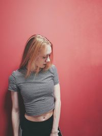 Beautiful young woman standing against red wall