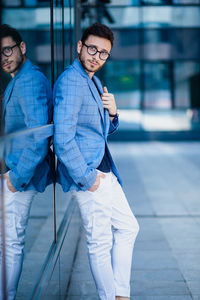 Full length portrait of young man leaning on glass wall