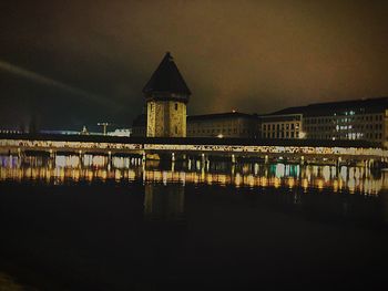 Illuminated building by river against sky at night