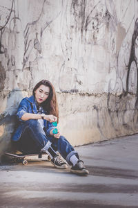 Young woman sitting against wall