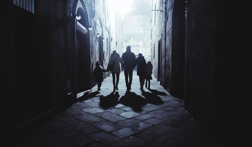 Rear view of silhouette people walking in alley amidst buildings