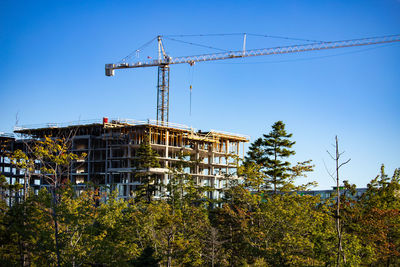 Low angle view of crane at construction site against clear blue sky