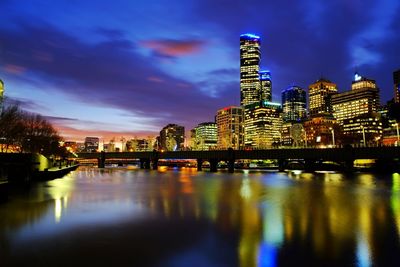 Illuminated city by river against sky at night