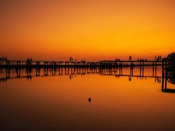 Silhouette pier over sea against orange sky