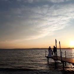 Silhouette people standing on sea against sky during sunset